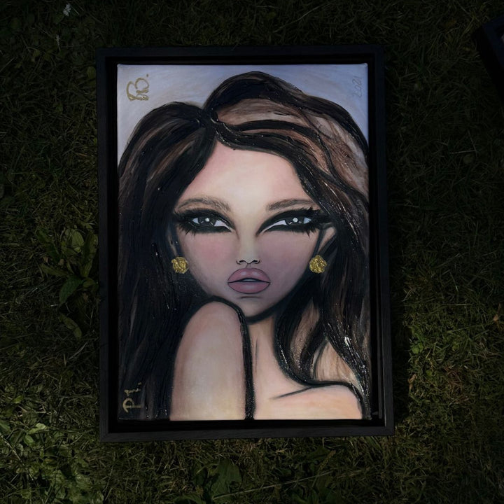 A framed portrait painting of a stylized woman with dark hair, dramatic eyes, and gold earrings, placed on a dark grassy ground.